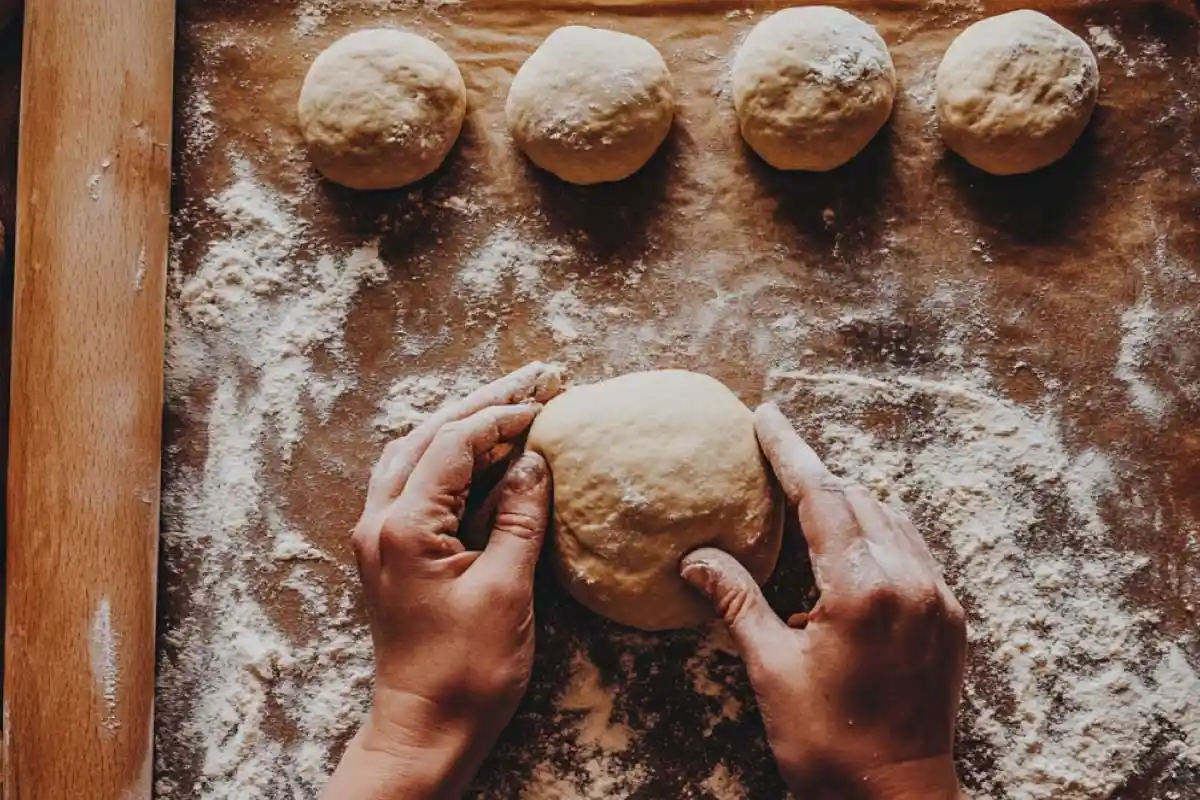 Shaping-Sourdough-Dough Hands shaping sourdough dough balls on a floured surface, with prepared dough balls in the background.