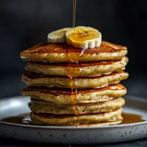 Fluffy sourdough discard banana pancakes stacked with syrup and fresh banana slices.