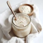 sourdough-tips-starter-closeup Close-up of a bubbly sourdough starter in a glass jar with baking tools.