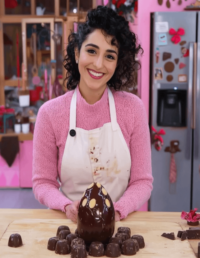 Olivia Baker smiling in her kitchen, wearing a flour-stained apron, presenting a chocolate pastry creation.